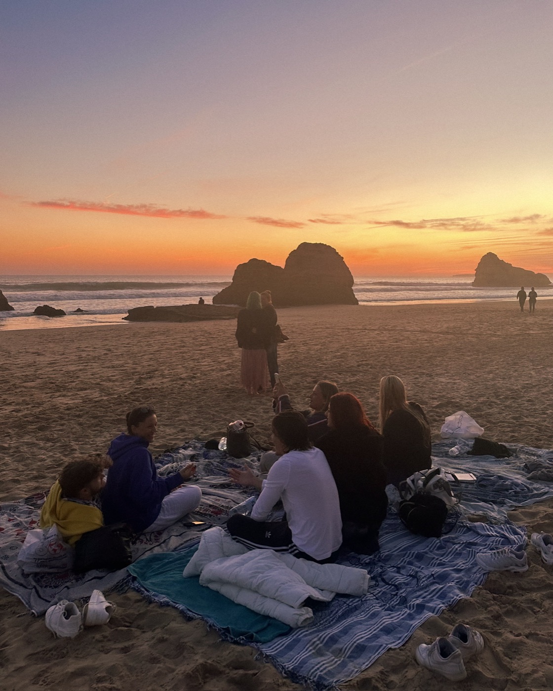 Die Gruppe sitzt bei Sonnenuntergang auf Decken am Strand