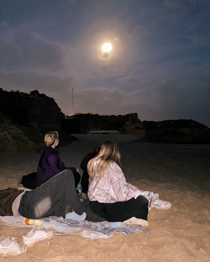 Zwei Freundinnen sitzen nachts am Strand unter dem Vollmond